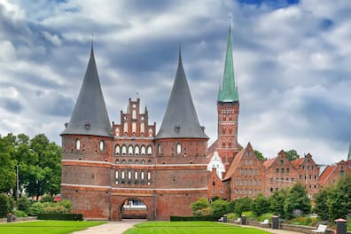 Holstentor in Lübeck aus Backstein und mit zwei Türmen, im Hintergrund weitere Backsteingebäude und ein Kirchturm mit grüner Spitze